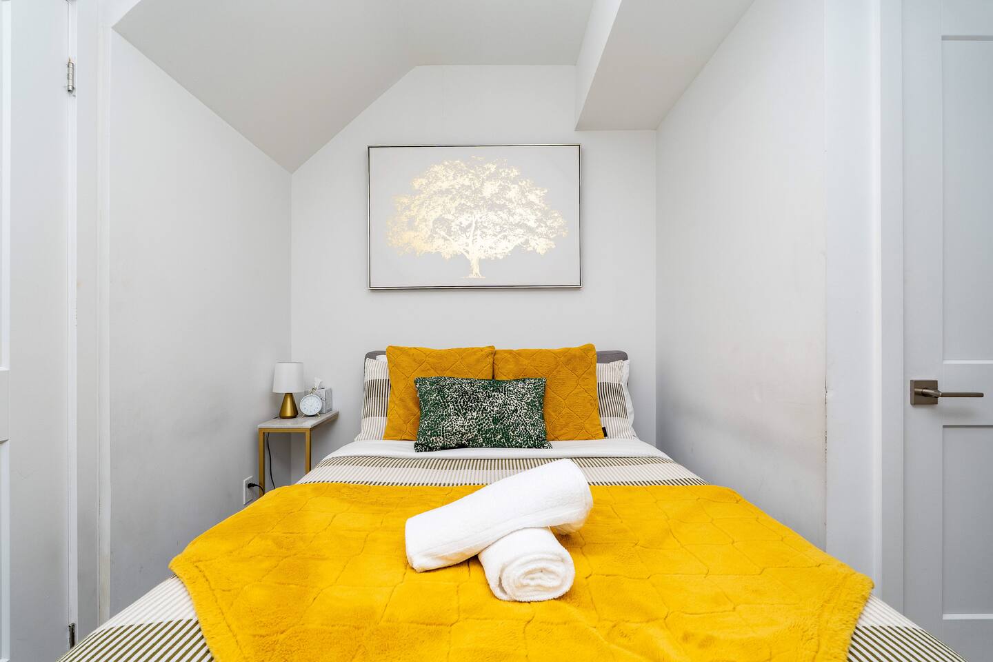 Bright bedroom with fresh linens, warm yellow accents, and bedside lighting, offering a clean and comfortable place to rest.
