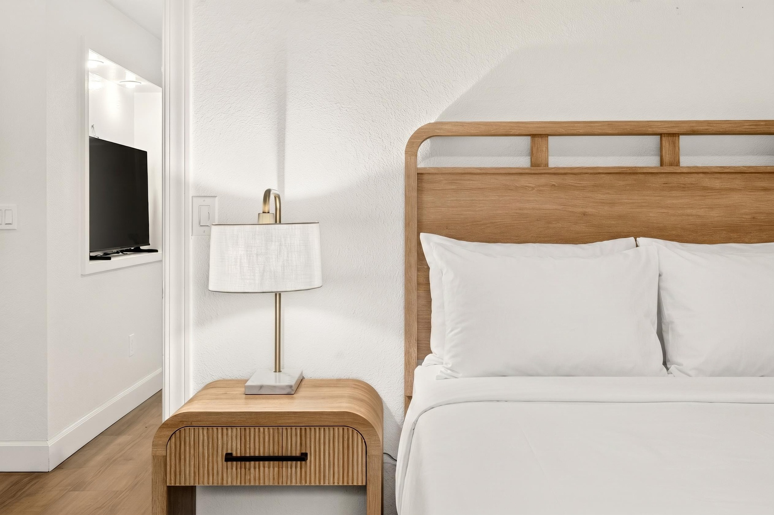 Bright minimalist bedroom with warm wood accents and plush white bedding