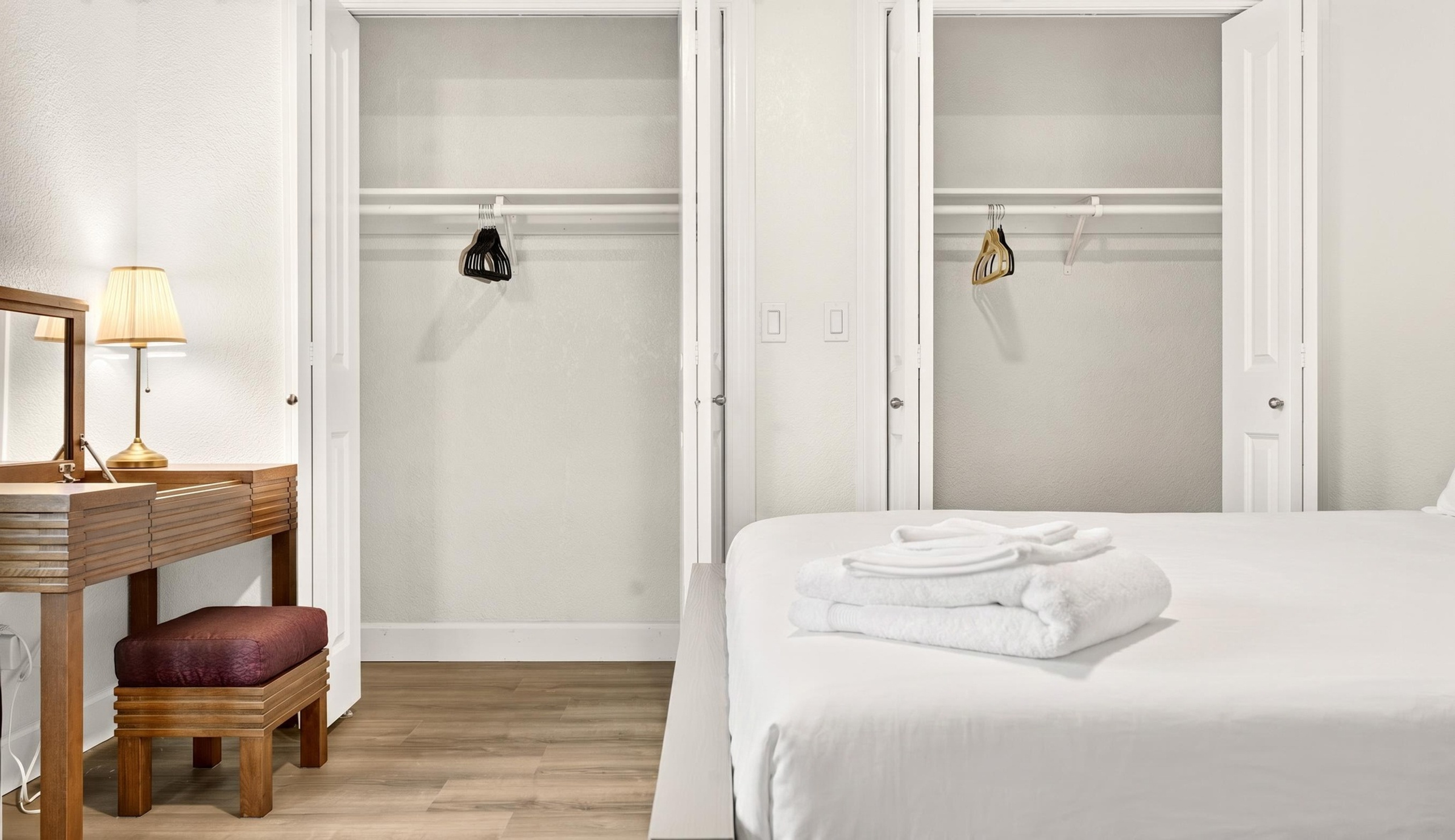 Bright bedroom with dual closets, vanity desk, and fresh linens