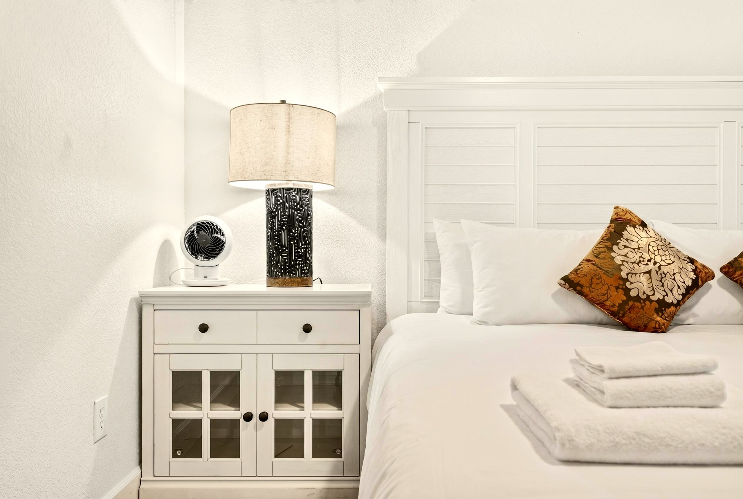 Bright, cozy bedroom with crisp linens, stylish lamp, and bedside storage