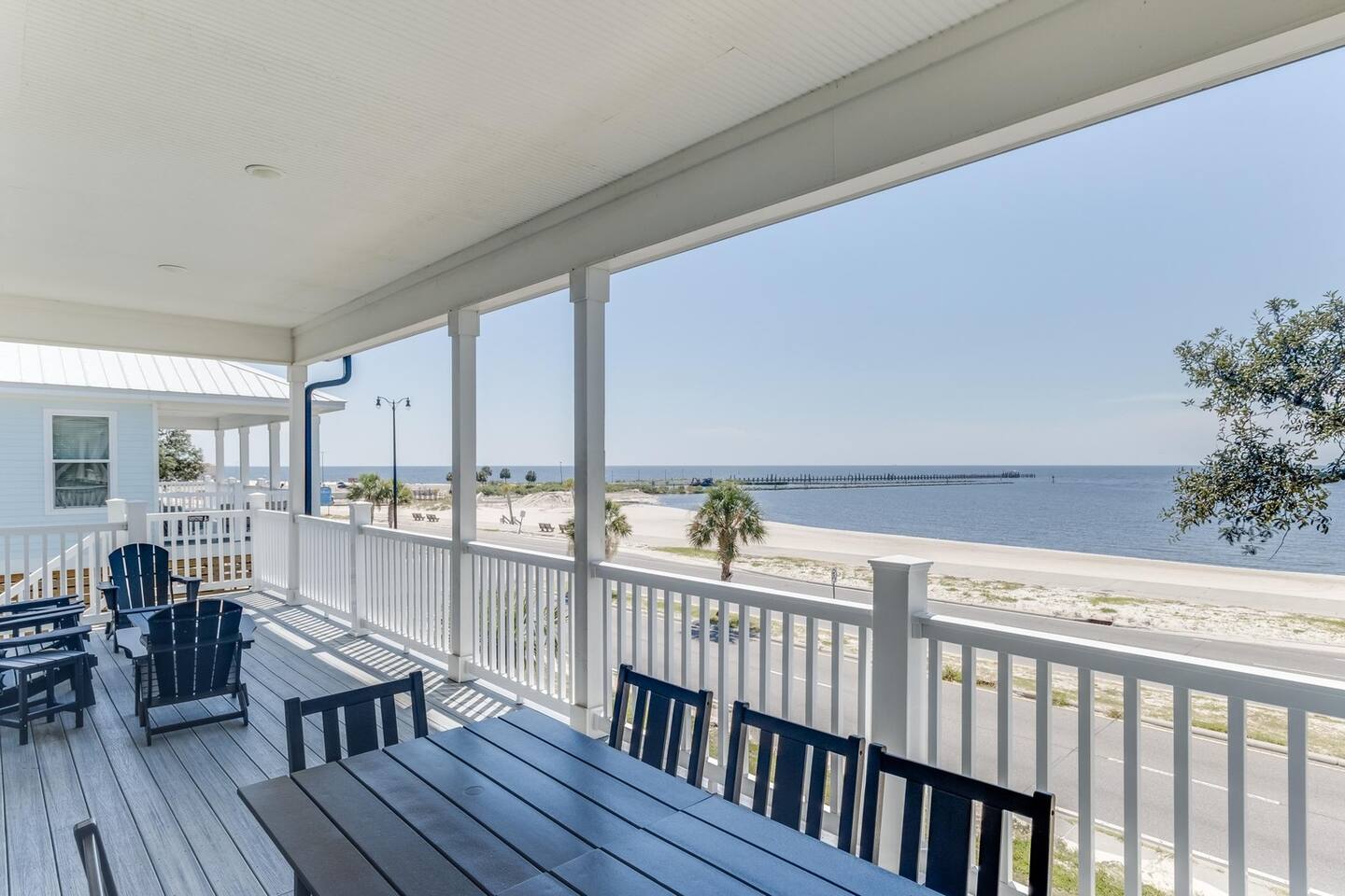 The covered front porch at White Breeze, with blue Adirondack chairs looking across Beach Boulevard to the sand and water in Gulfport