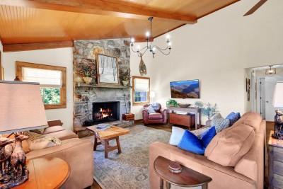 Gather in this luxury lodge-style living room, featuring a striking stone fireplace and soaring vaulted wood ceilings — the perfect warm, rustic space to relax and reconnect after a day in the mountains.
