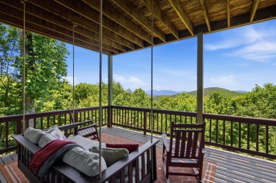Relax on the covered deck featuring a swing bed and rocking chair perfectly positioned to soak in stunning long-range mountain views — the ultimate spot for morning coffee or sunset evenings.