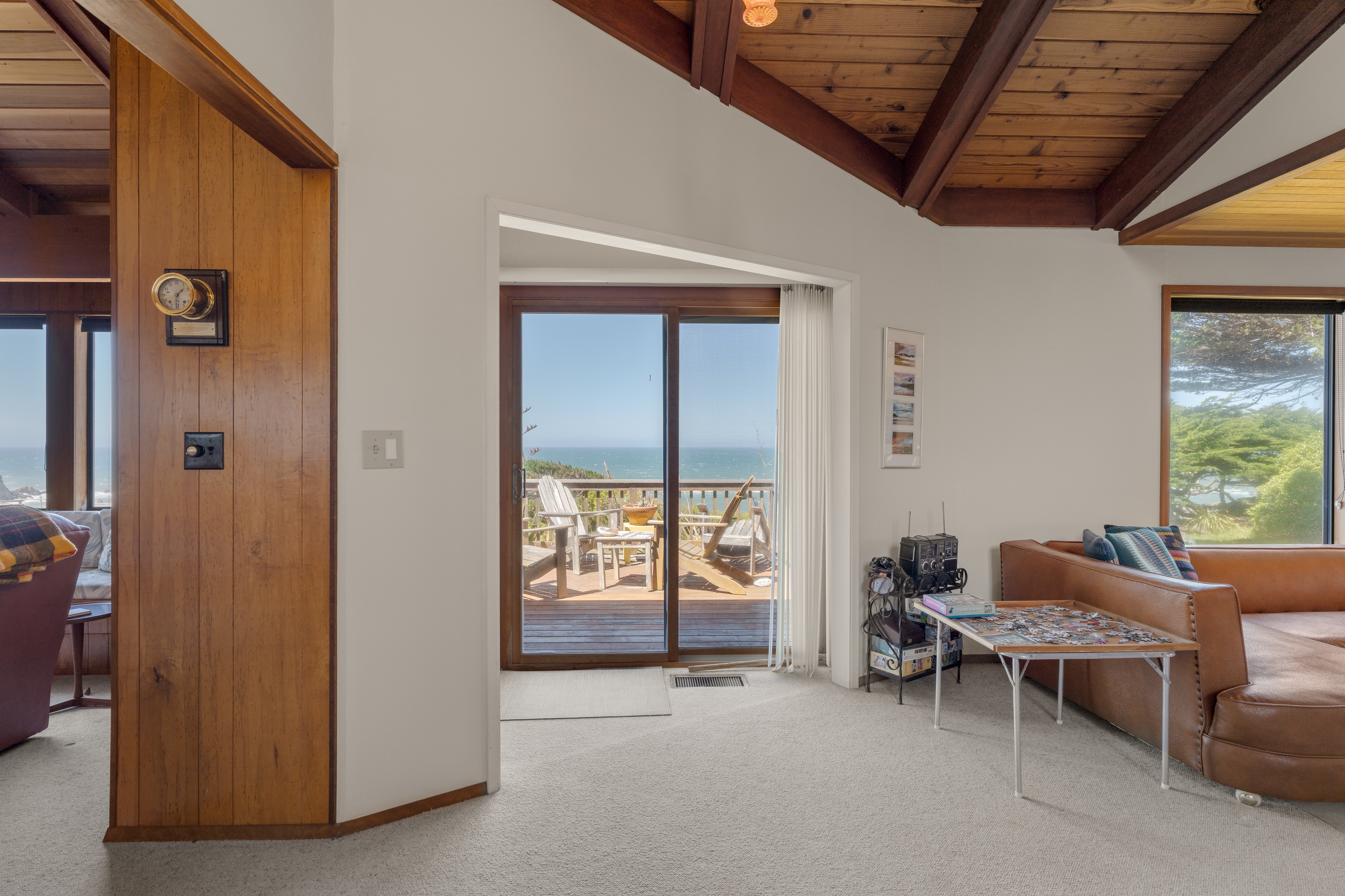 Bright living room with vaulted ceilings, deck access, and ocean views