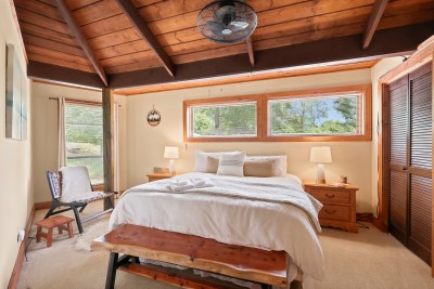 The main floor king bedroom impresses with soaring vaulted wood ceilings and bright garden views — a warm and inviting retreat perfect for relaxing after a day of mountain adventures.