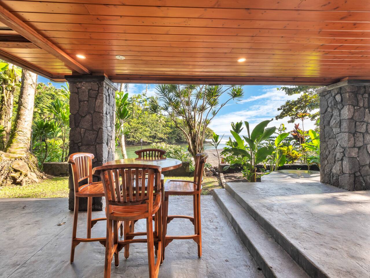This outdoor dining area, with its table for four, is an ideal spot to enjoy a meal while surrounded by the lush landscape and calming ocean breeze.