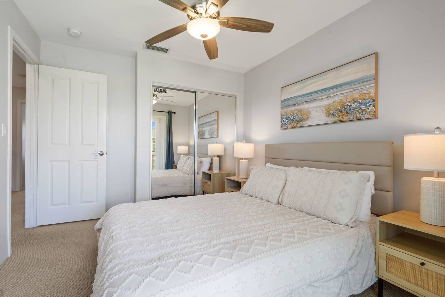 Bright and serene bedroom featuring mirrored closet doors, a cooling ceiling fan, and blackout curtains for a comfortable, restful stay.
