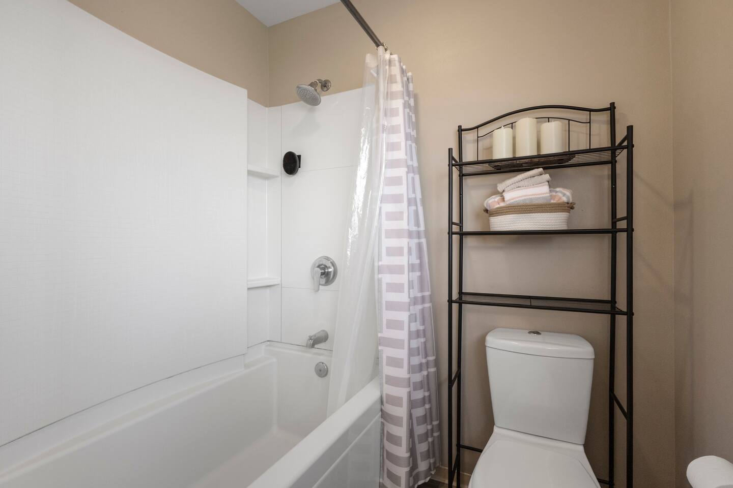 Clean and simple bathroom with a full tub-shower combo and convenient shelving for extra storage.