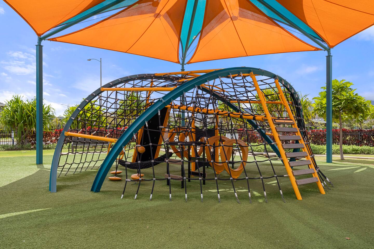 Contemporary playground with climbing nets, curved bars, and a colorful canopy over soft turf.