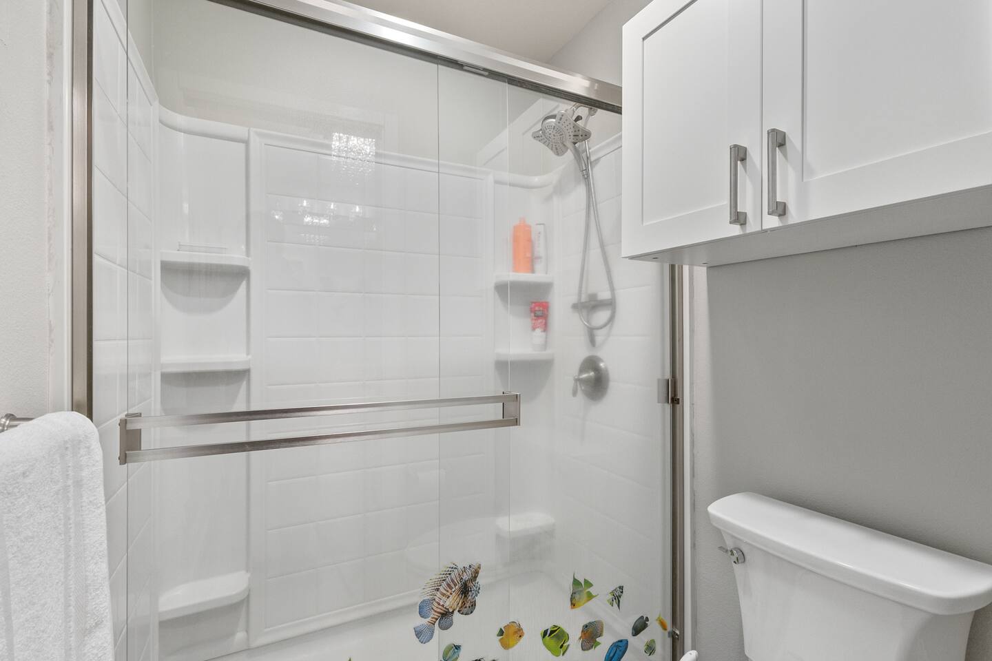 Modern bathroom with glass-enclosed shower, built-in shelving, and upper cabinet storage above the toilet.