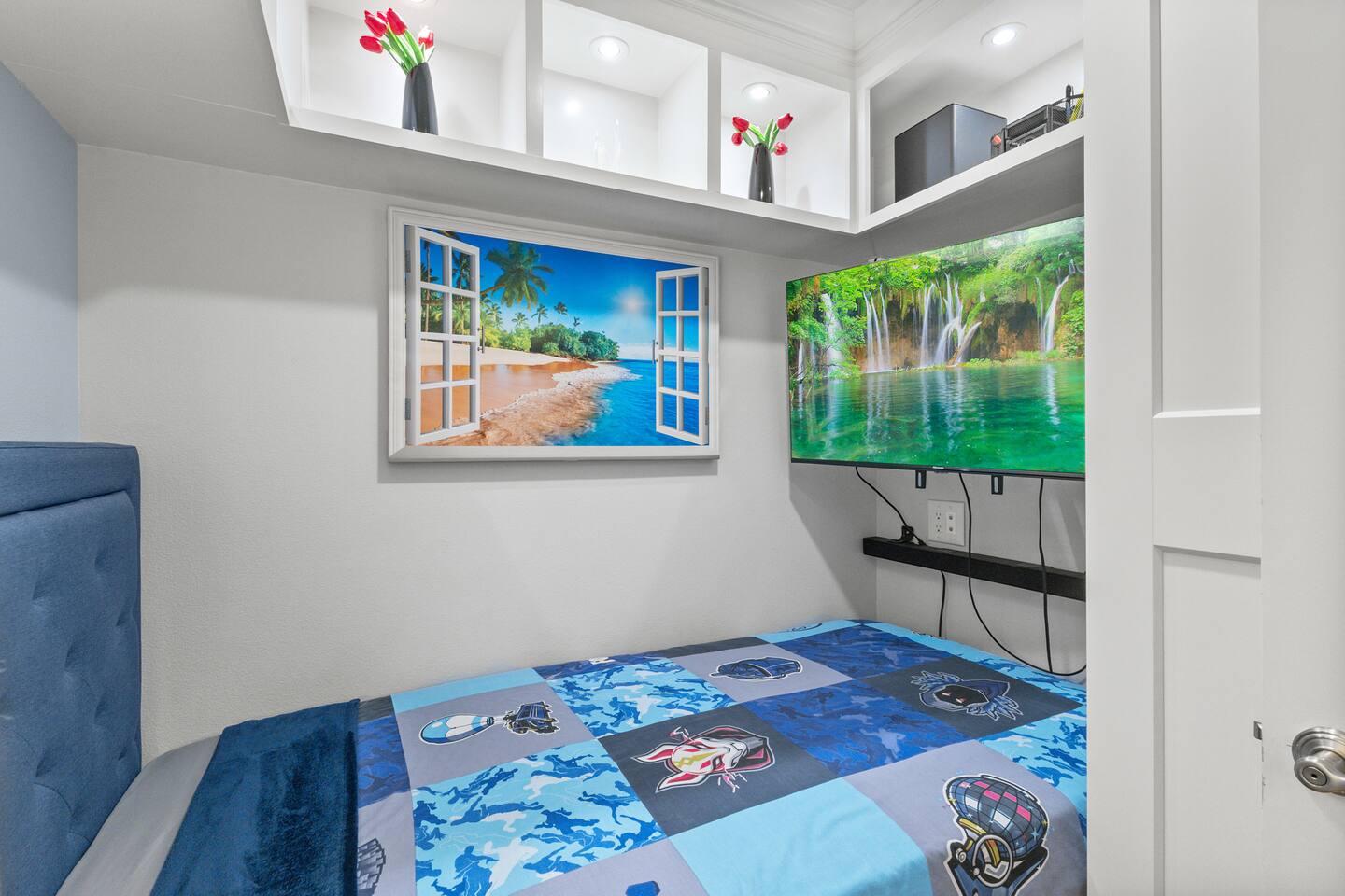Compact bedroom with wall-mounted TV, recessed shelving, and a faux window art piece for added charm.
