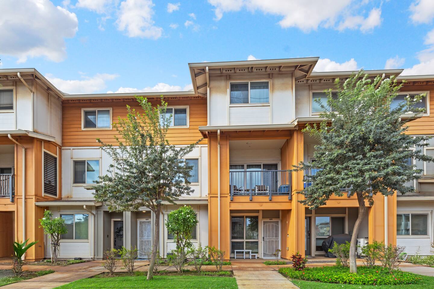 Three-story apartment with balconies, landscaped entry, and a mix of white and warm-toned siding.