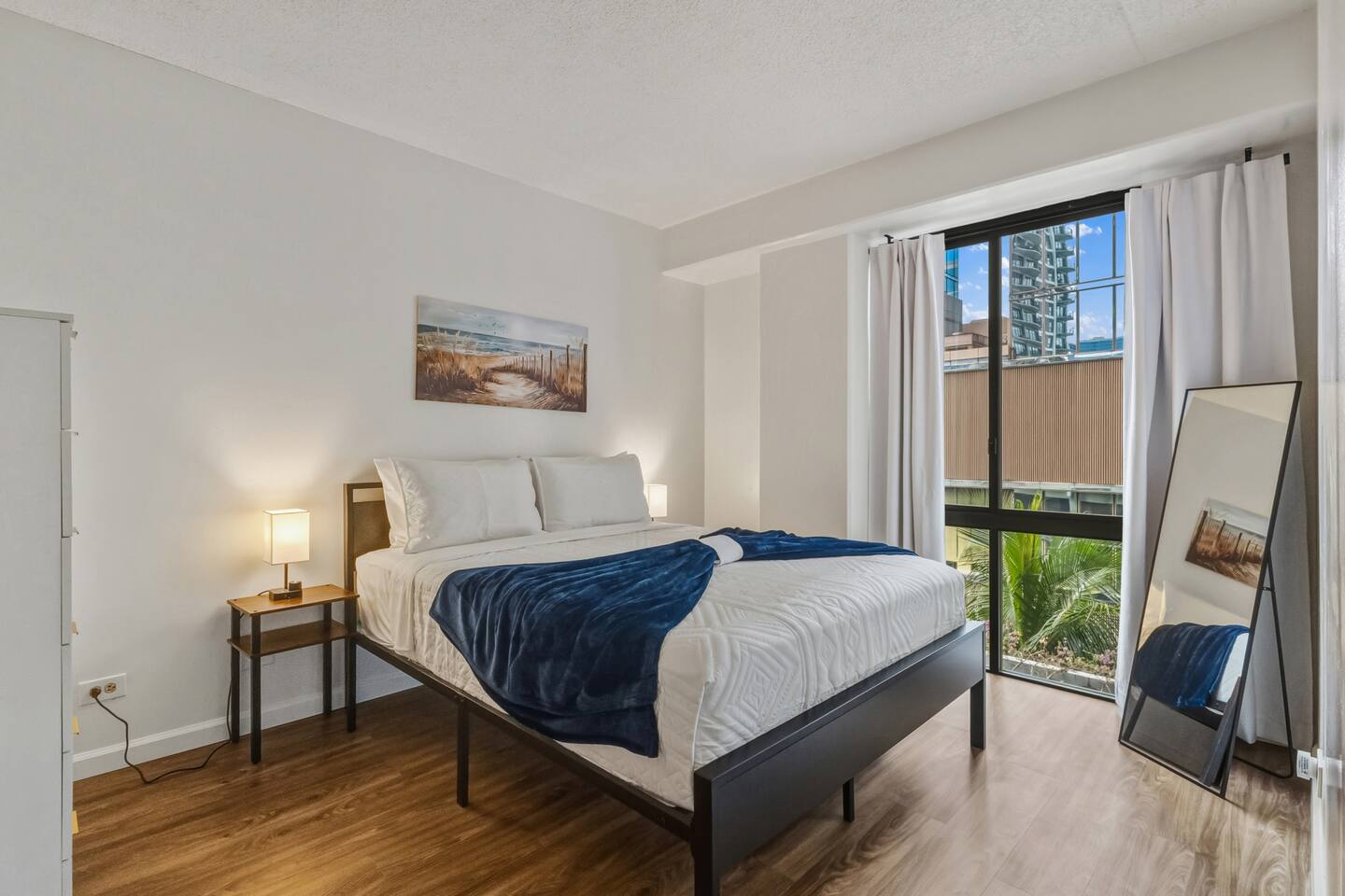 Coastal calm with city views. Soft linens, ocean art, and sunshine make this bedroom a peaceful retreat.