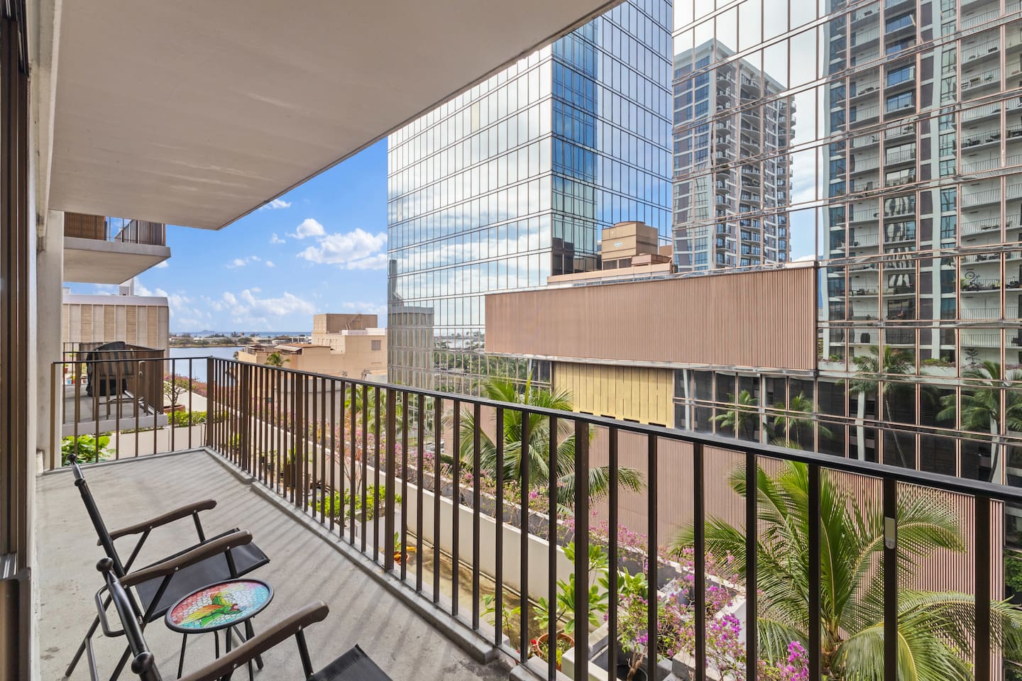 Urban calm with a colorful twist, where folding chairs and flowers meet glass towers and blue skies.
