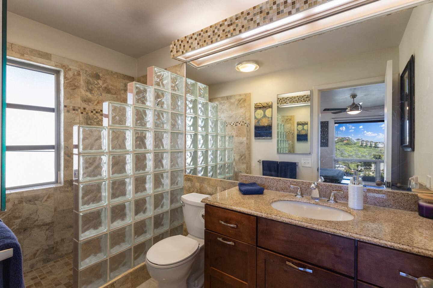 Travertine tile bathroom, combined with chic glass-block make for convenience and privacy in the spacious primary bath shower.