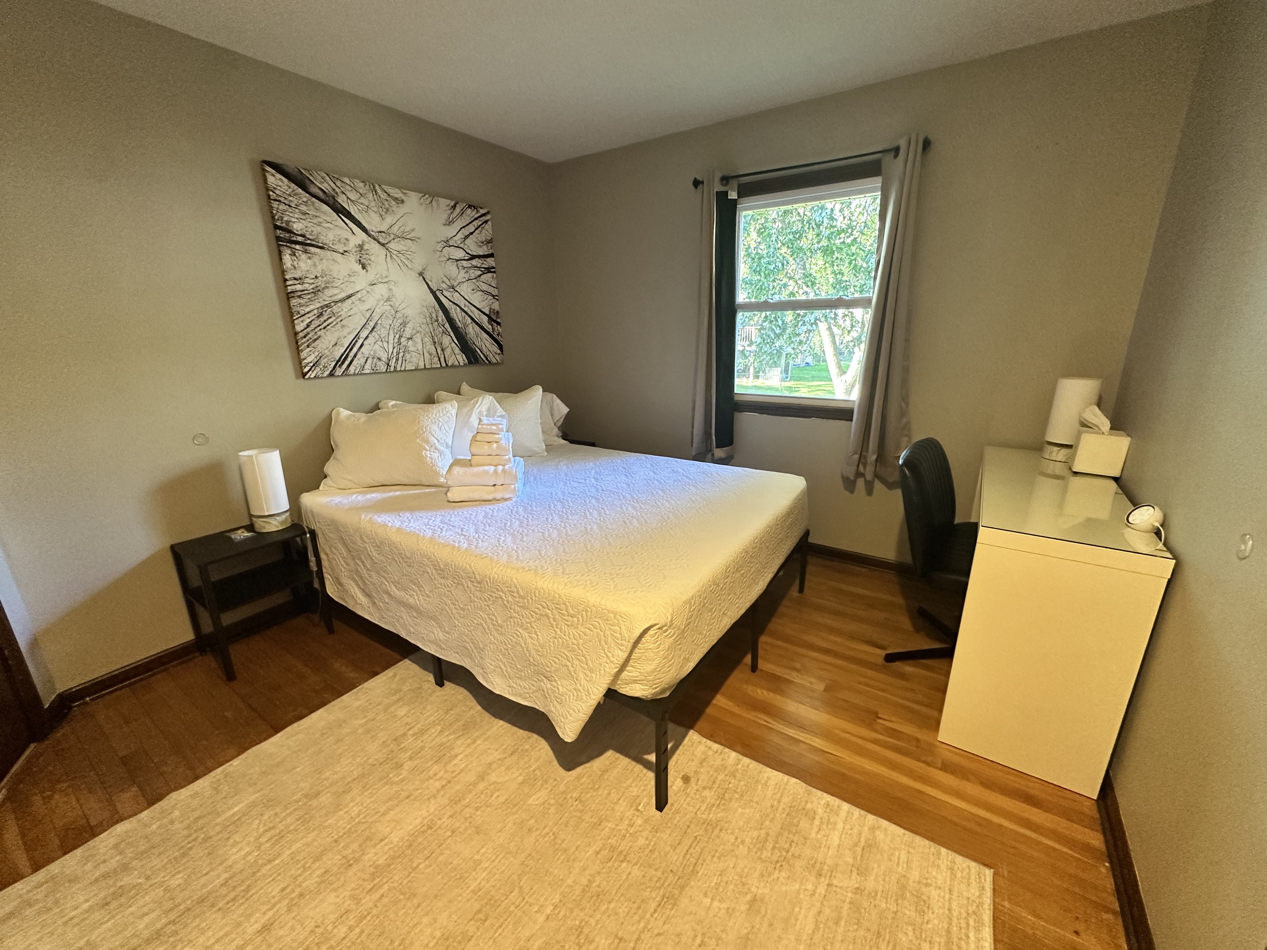 Bright, cozy bedroom with workspace and peaceful leafy views