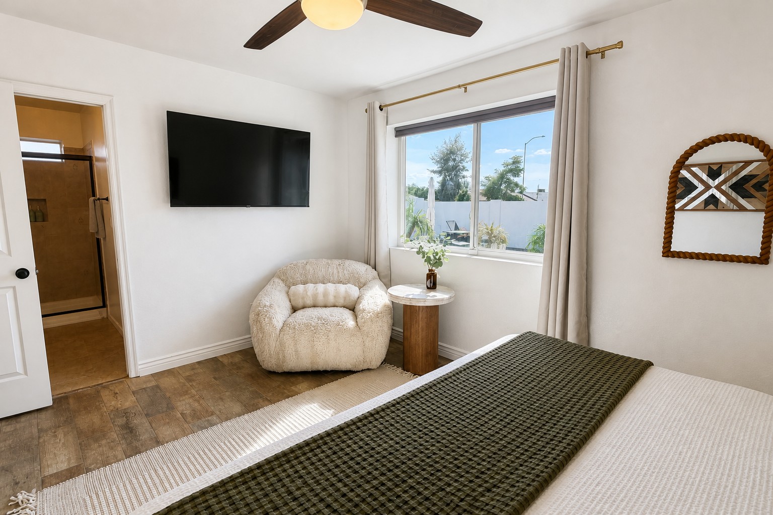 Bright bedroom with natural light, TV, cozy chair, and ensuite bath
