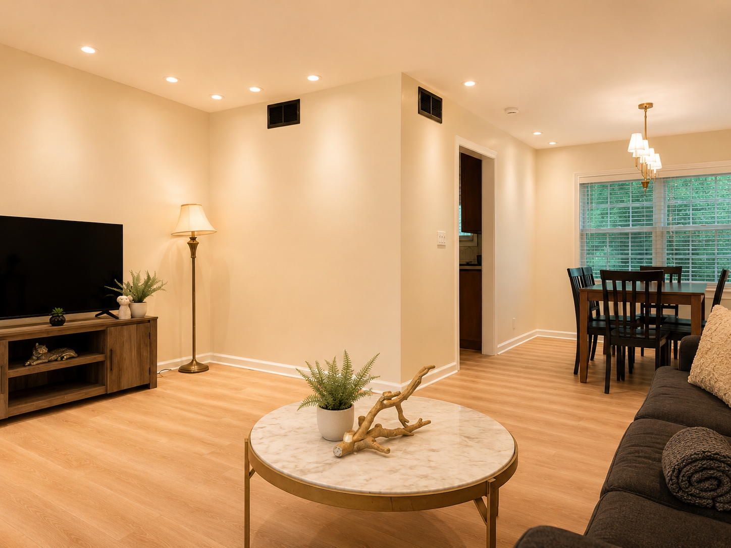 Bright open living & dining space with warm lighting and large window views