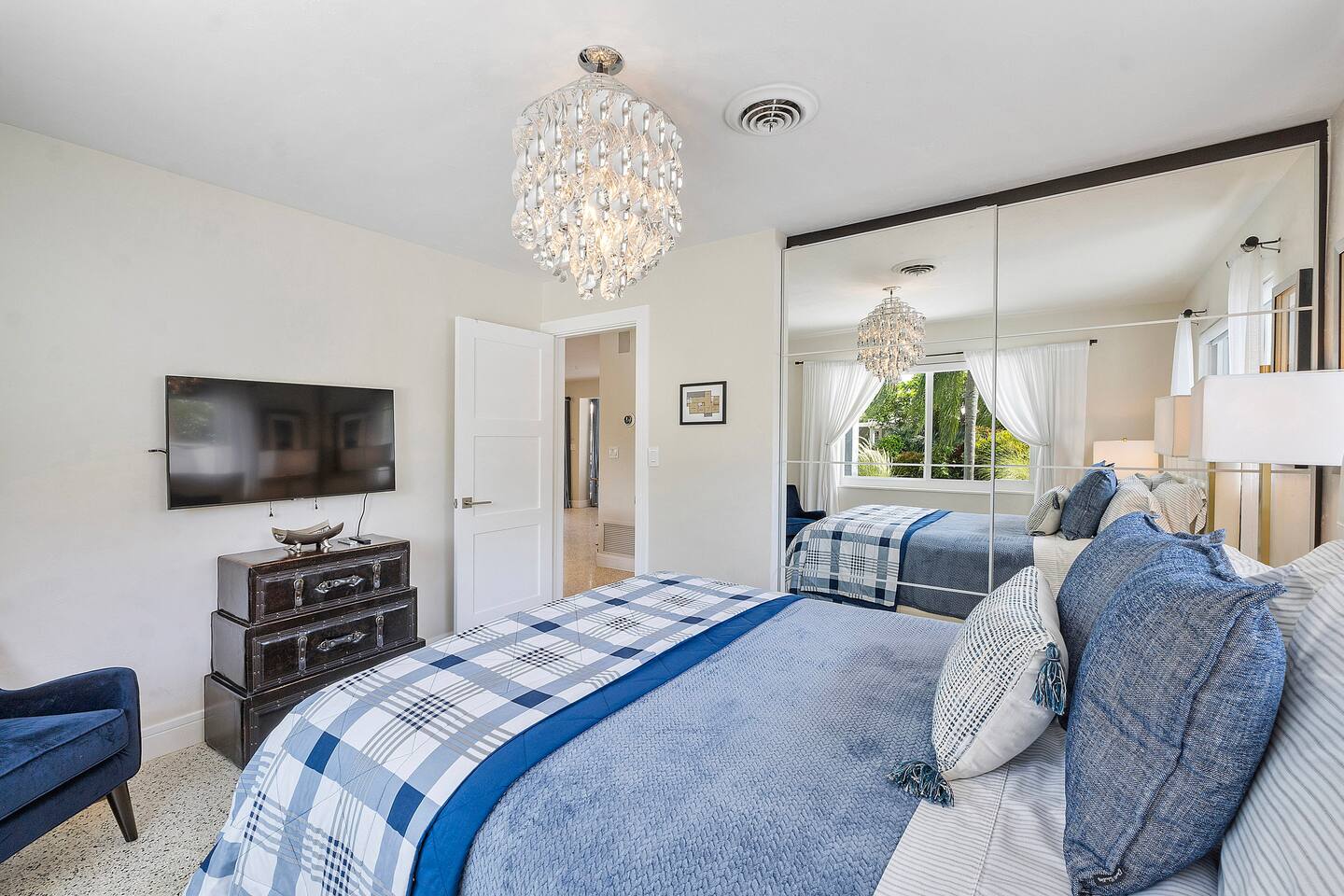 Rest comfortably in Bedroom 2, featuring a plush queen-size bed, elegant chandelier, Smart TV, and expansive windows that fill the room with natural light.