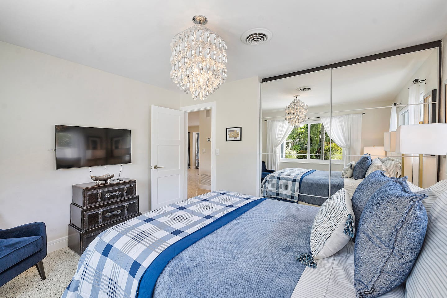 Rest comfortably in Bedroom 2, featuring a plush queen-size bed, elegant chandelier, Smart TV, and expansive windows that fill the room with natural light.