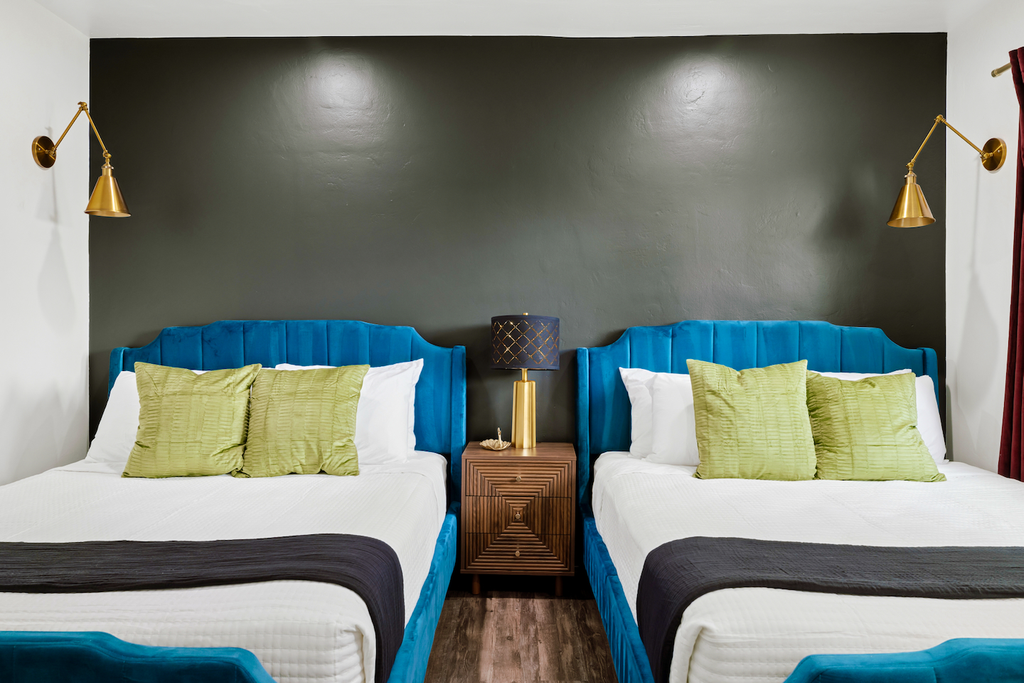 Two queen beds with teal velvet headboards and black accent wall