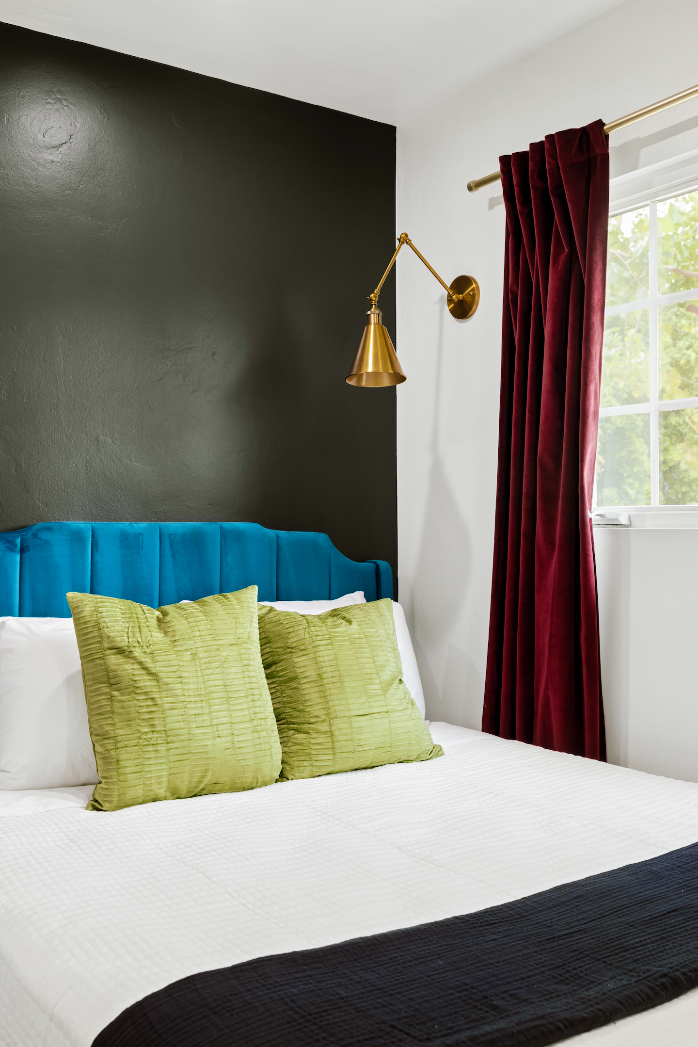 Queen bed with teal velvet headboard and brass wall sconce