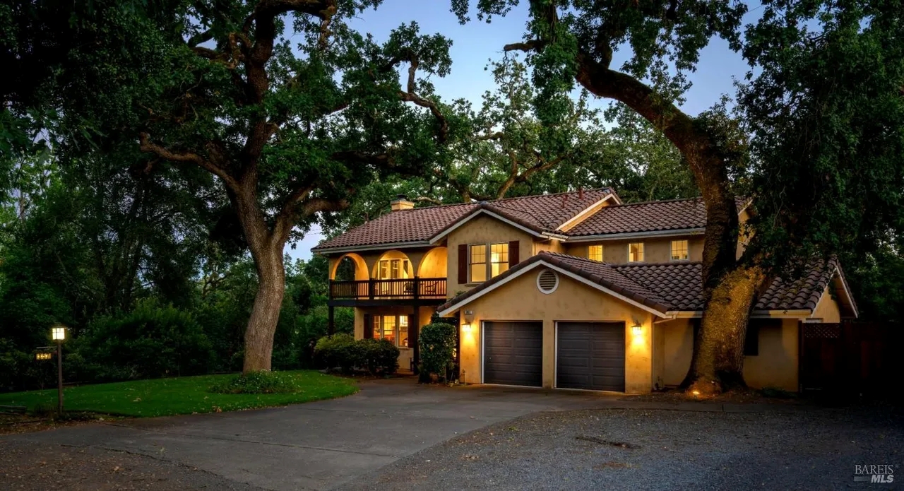Charming tree-lined retreat with warm lighting, balcony, and spacious drive