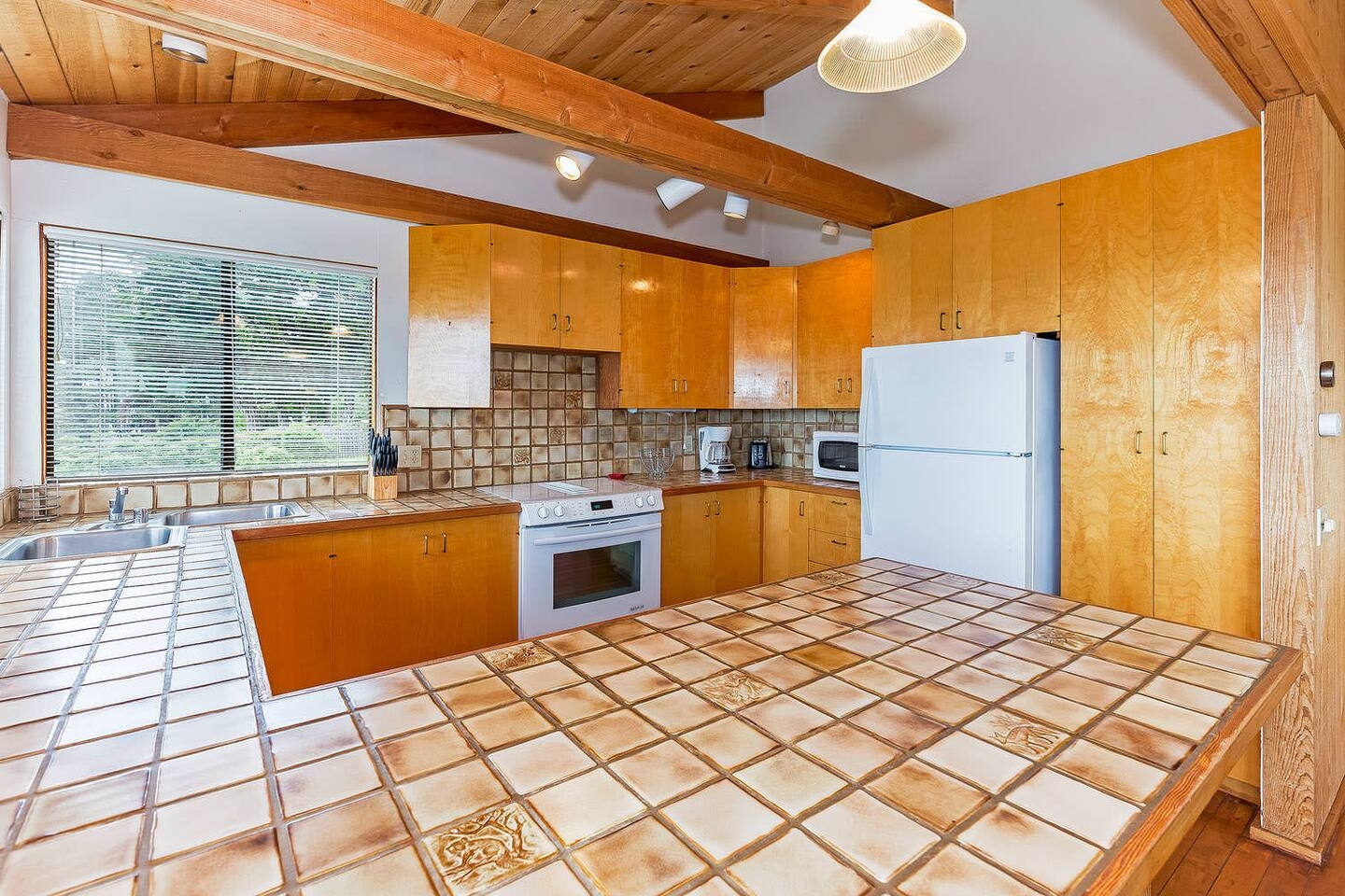 Rustic wood-beam kitchen with large tiled island and bright natural light