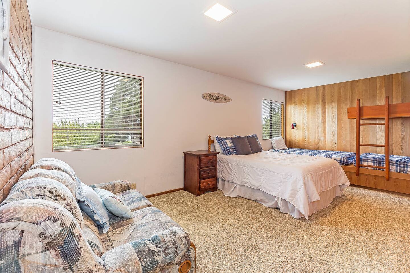 Spacious family bedroom with queen bed, bunks, sofa, and natural light