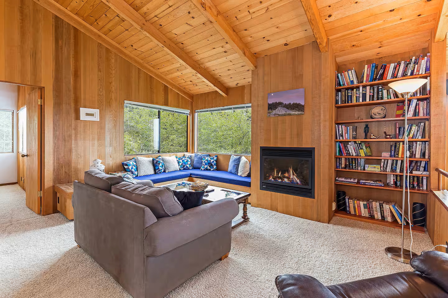 Cozy woodsy living room with fireplace, window seat, and forest views