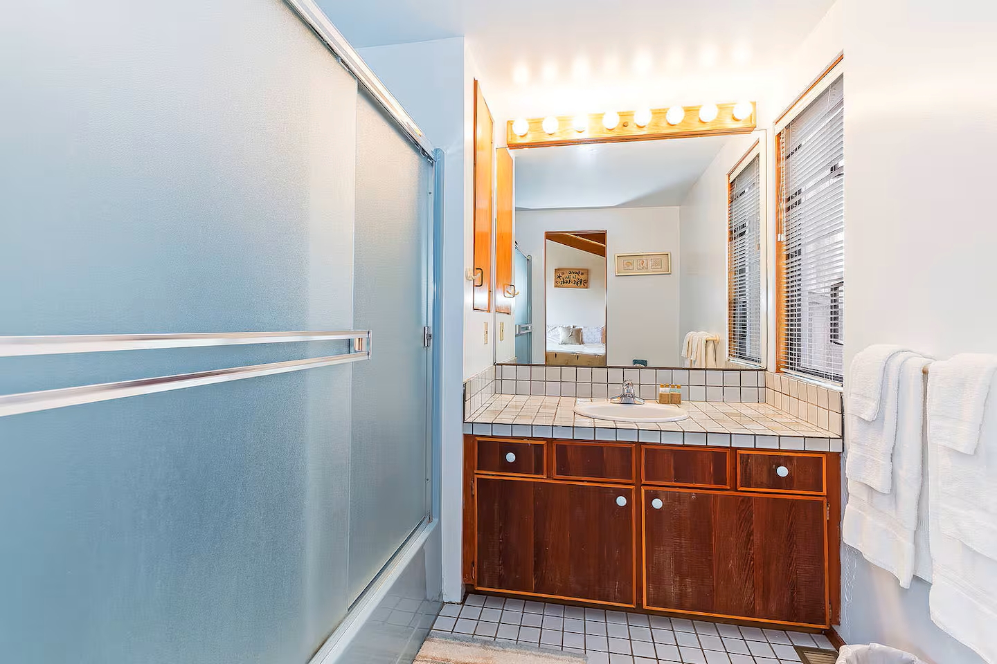 Bright bathroom with large vanity, warm wood cabinets, and glass shower