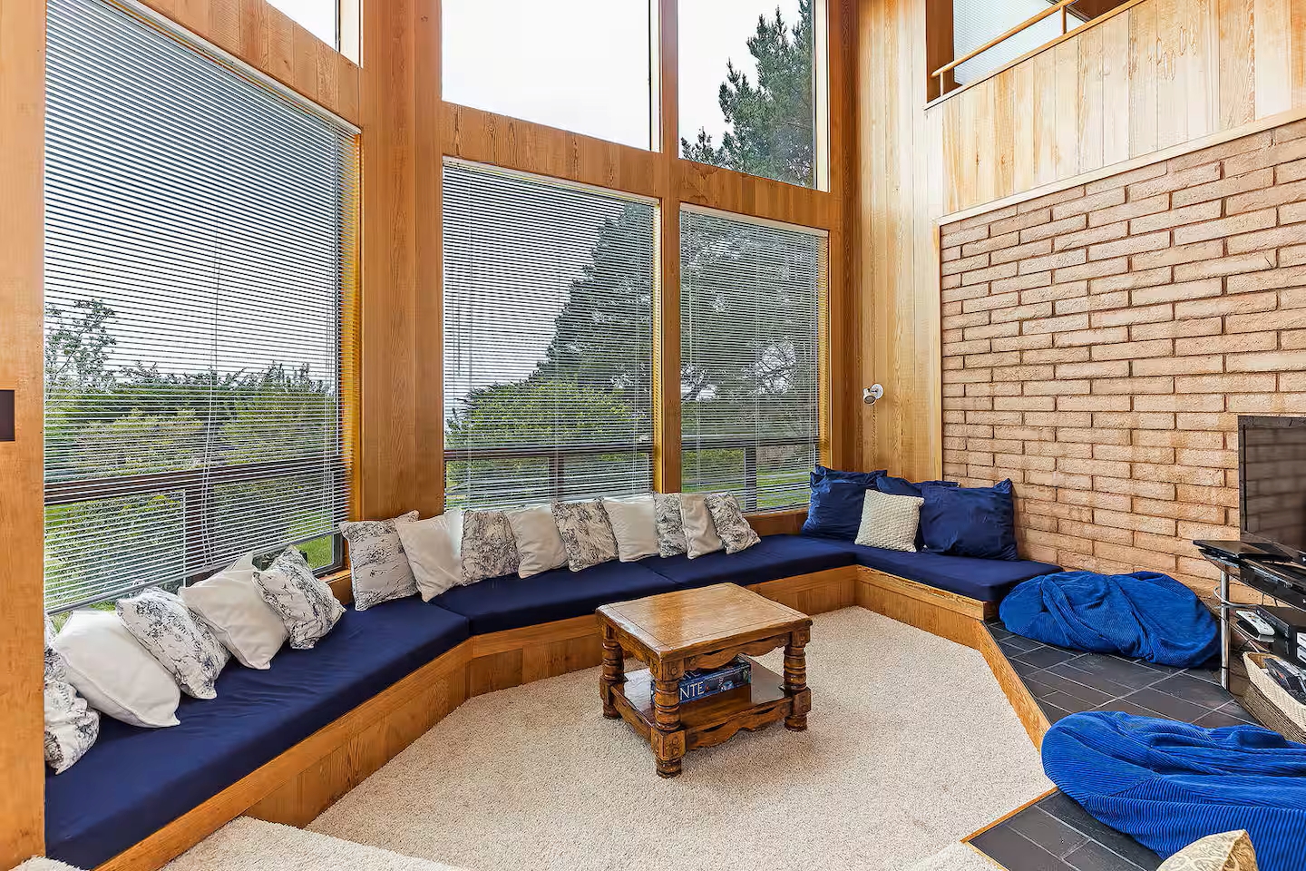 Sunlit lounge with wraparound seating, fireplace, and scenic forest views