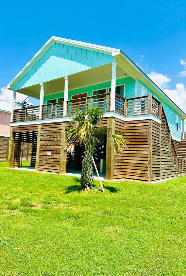 Cajun Paradise exterior, a mint green raised beach house with a palm tree