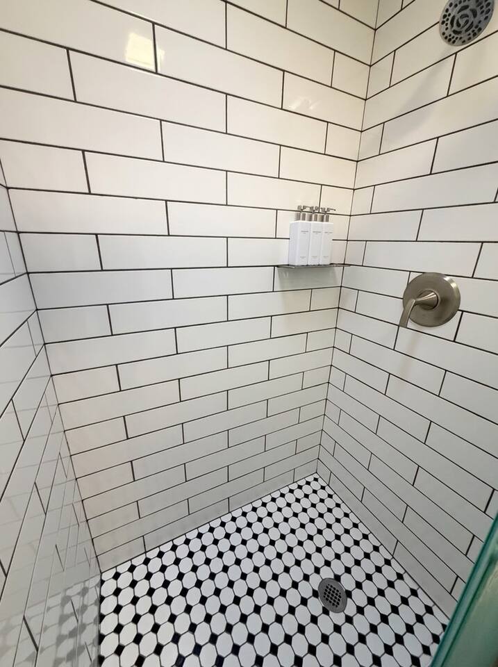 This newly remodeled full bathroom features a sleek walk-in shower with classic white subway tile, a stylish vanity with modern fixtures, and classic black-and-white patterned tile flooring for a refreshed, functional design.