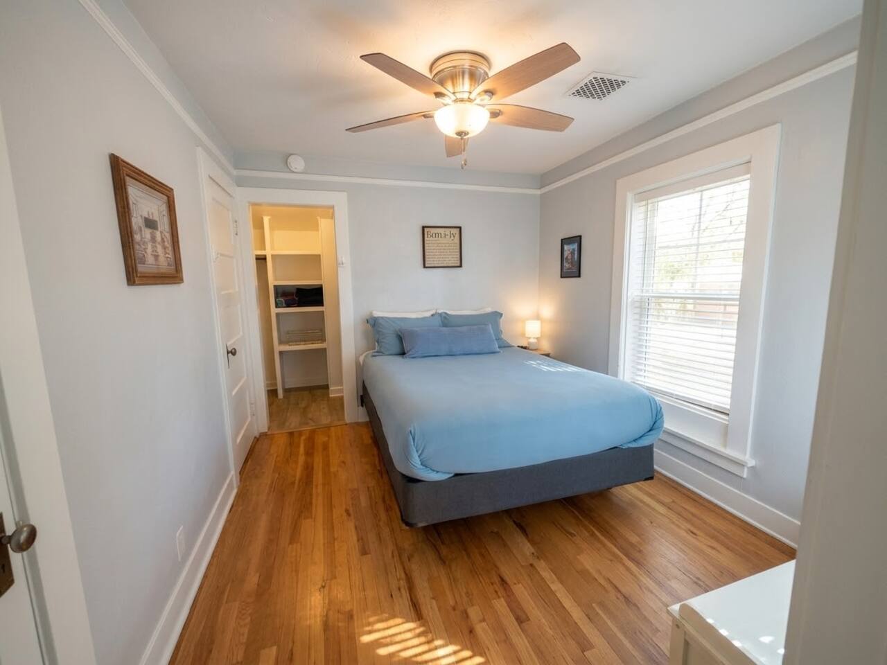 This peaceful bedroom features a comfortable queen bed, warm hardwood floors, and a ceiling fan. Bathed in natural light with ample closet storage, it offers a cozy and restful retreat for guests.