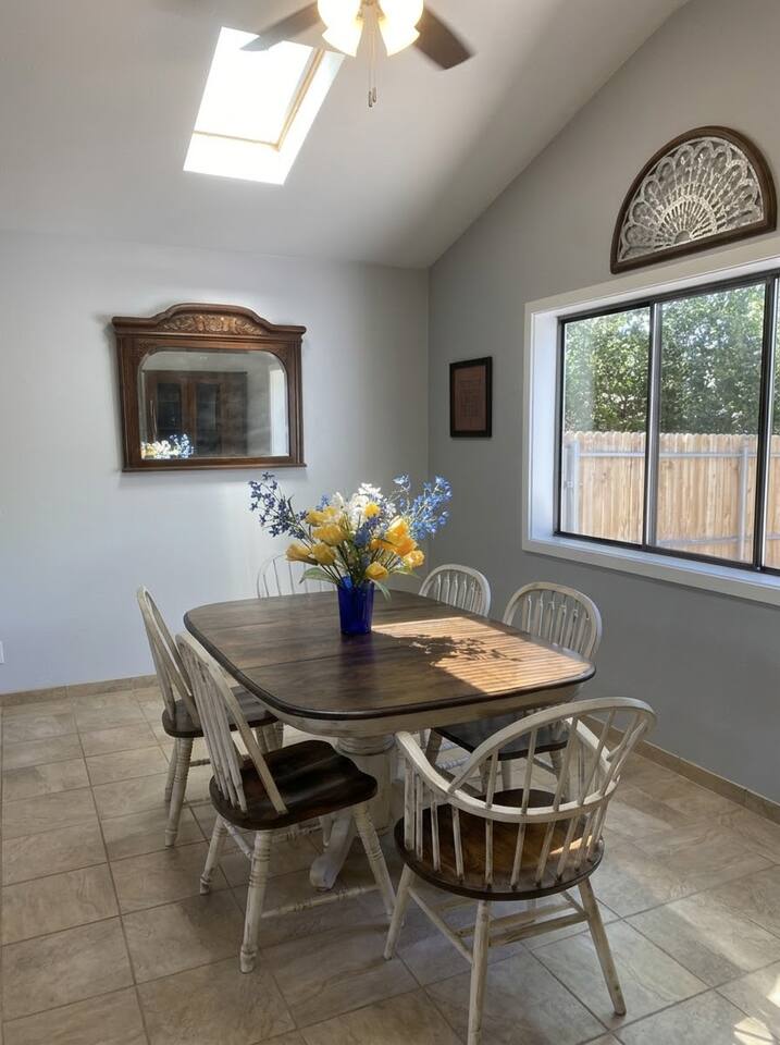 The dining area features a classic wooden table with matching chairs, tile flooring, and ample natural light. Accentuated by a vintage wooden hutch and decorative touches, it creates an inviting space for sharing meals.