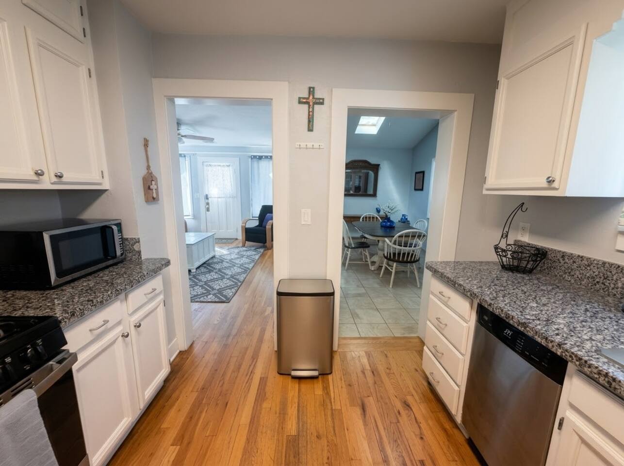 The full kitchen features bright white cabinetry, sleek granite countertops, stainless steel appliances, and rich hardwood floors. Fully equipped with modern essentials, it offers a warm, functional space for preparing meals.