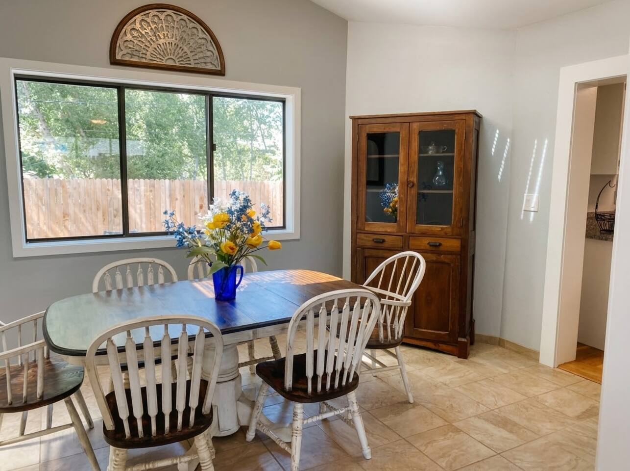 The dining area features a classic wooden table with matching chairs, tile flooring, and ample natural light. Accentuated by a vintage wooden hutch and decorative touches, it creates an inviting space for sharing meals.