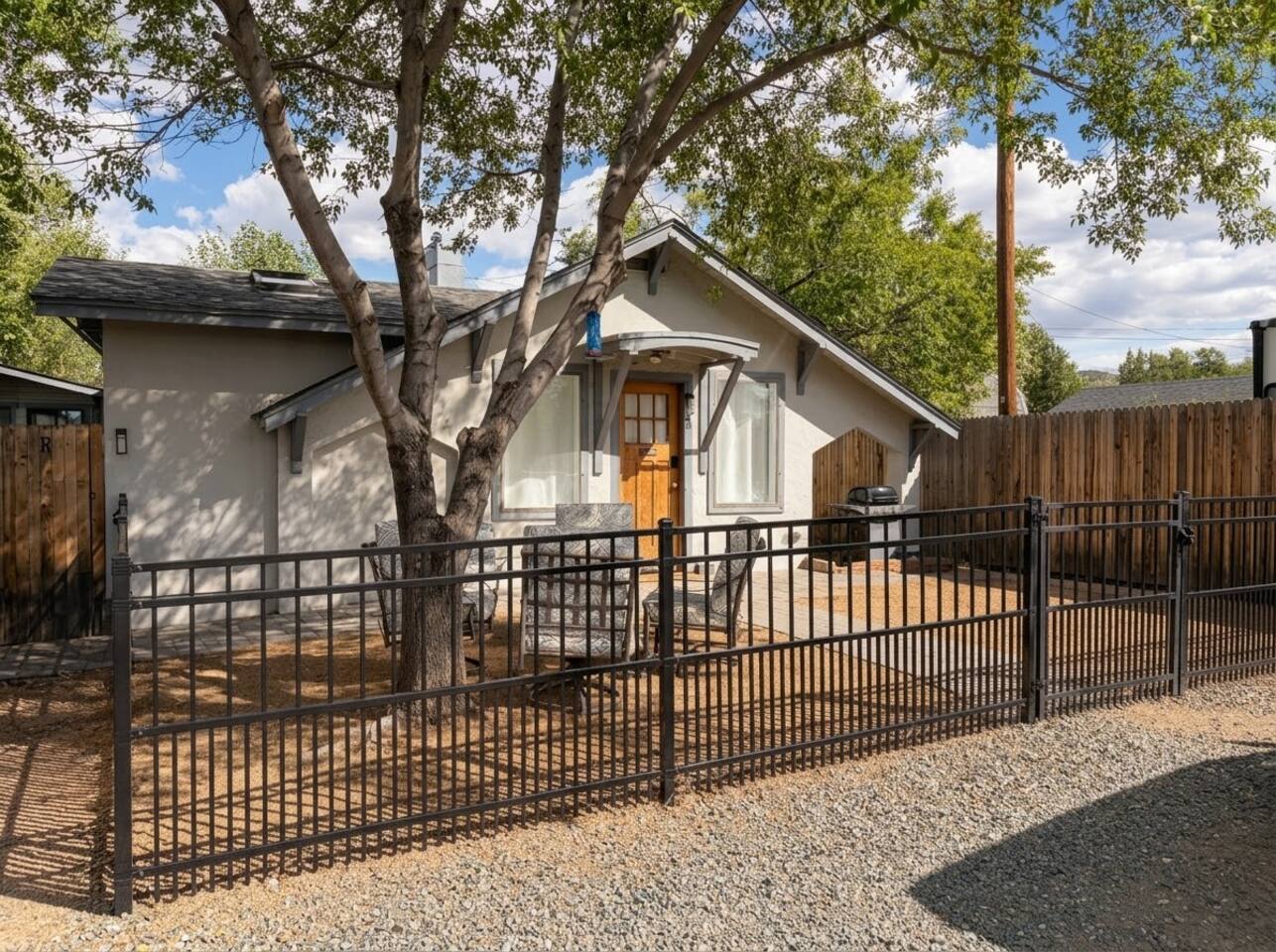The single-story exterior features a charming stone-accented facade, a classic wooden front door, and mature shade trees. Highlighted by lush natural landscaping, a fenced yard, and a welcome mat entryway, it offers great curb appeal.