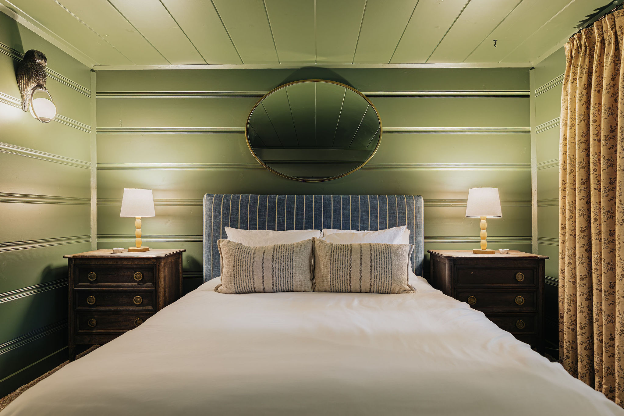 Cozy king bedroom with green paneled walls and warm designer touches