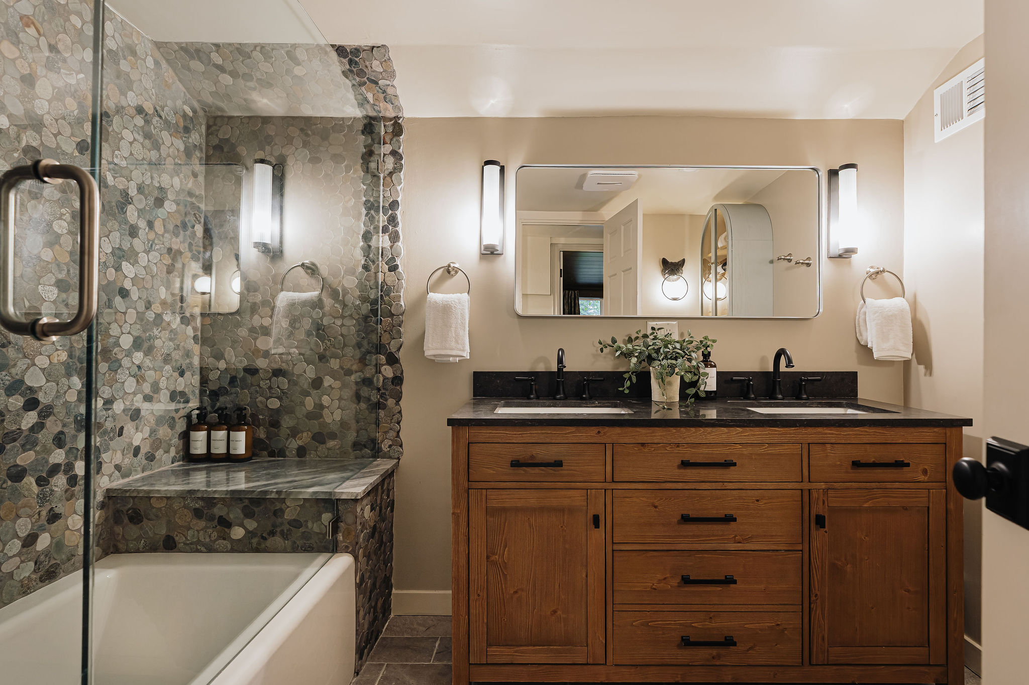 Spa-style bathroom with double vanity and elegant pebble-tile shower