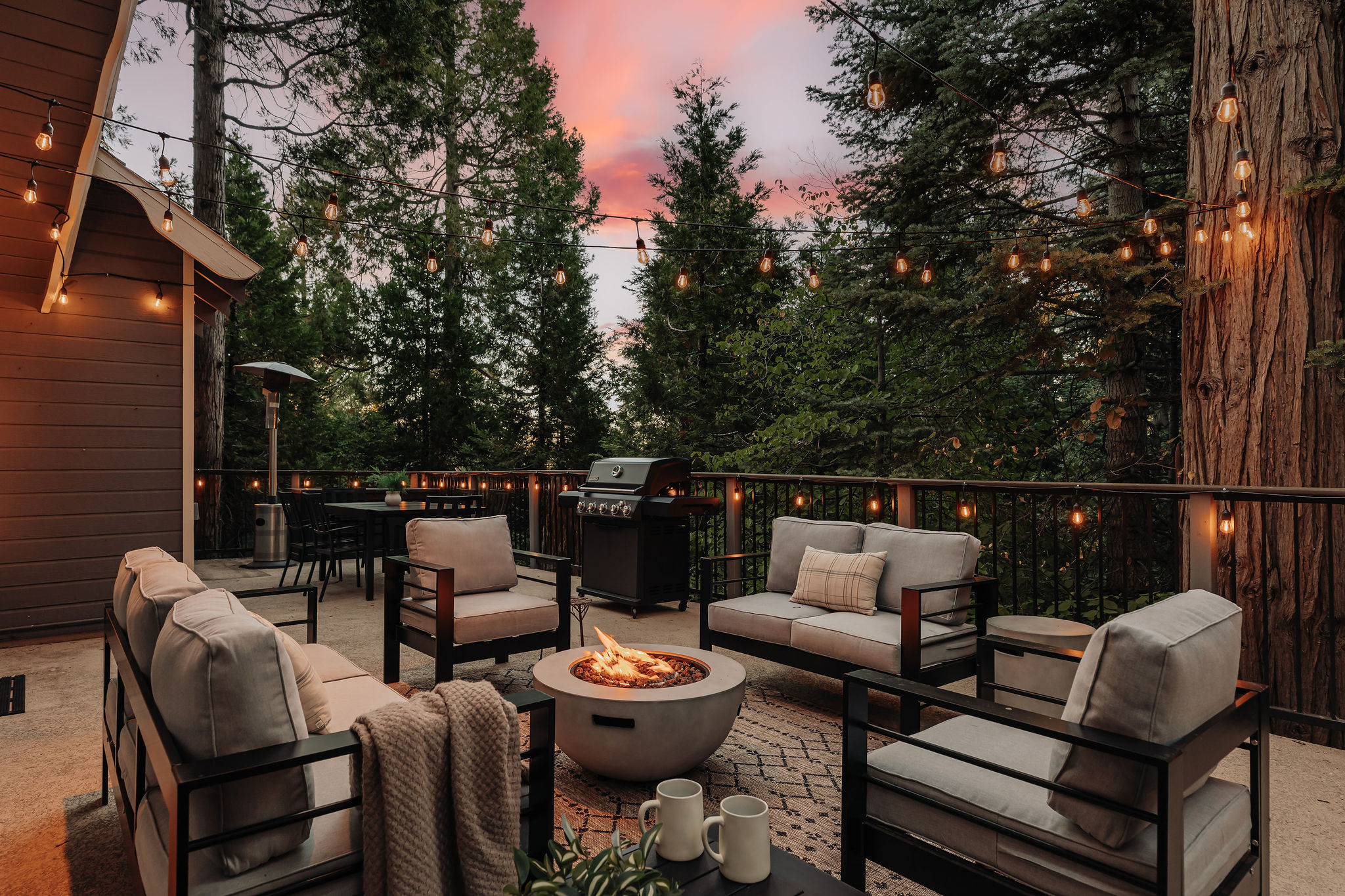 Forest-view deck with fire pit, grill, and glowing string lights