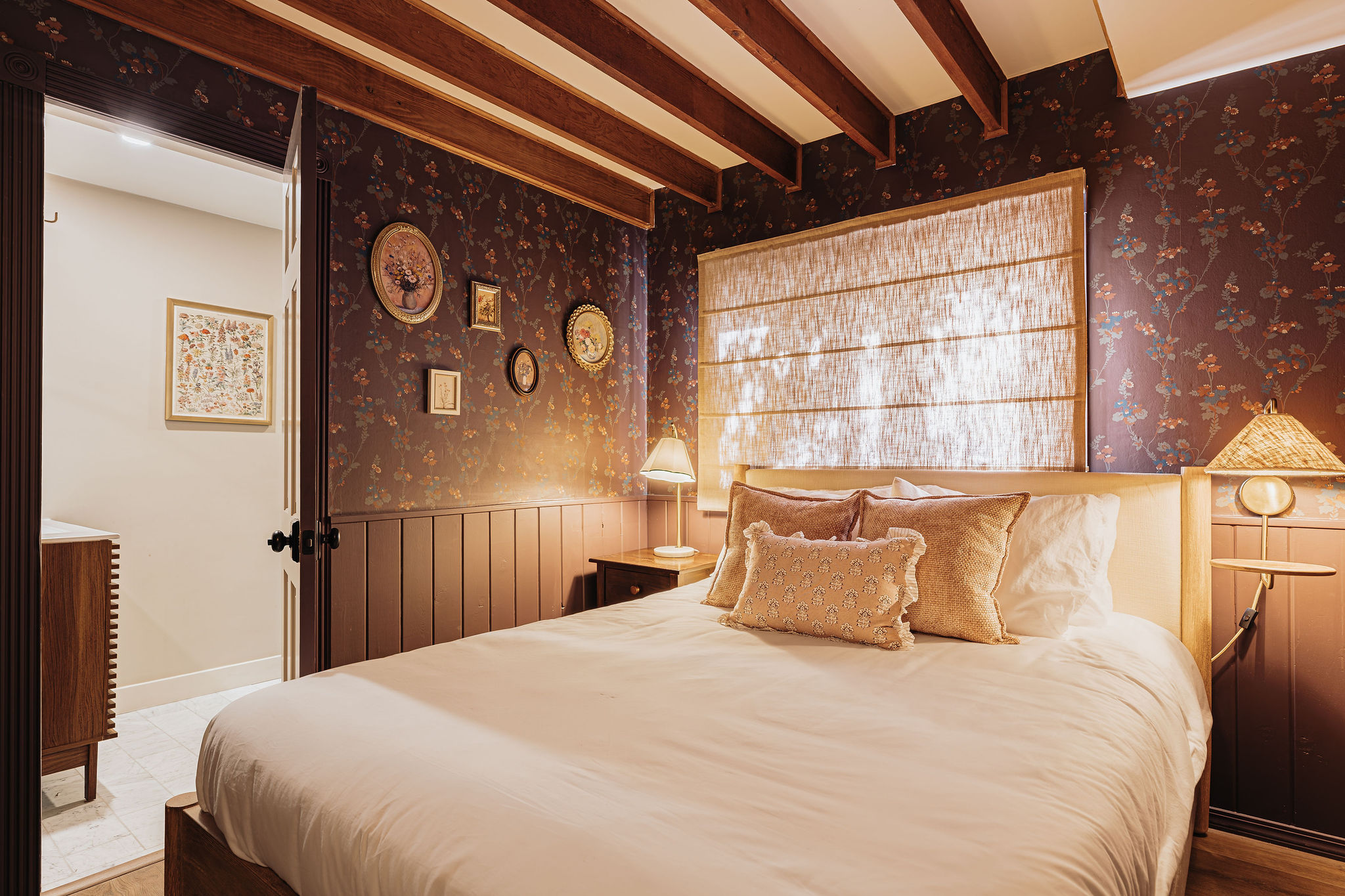 Charming bedroom with wood beams, floral walls, and a cozy, inviting bed