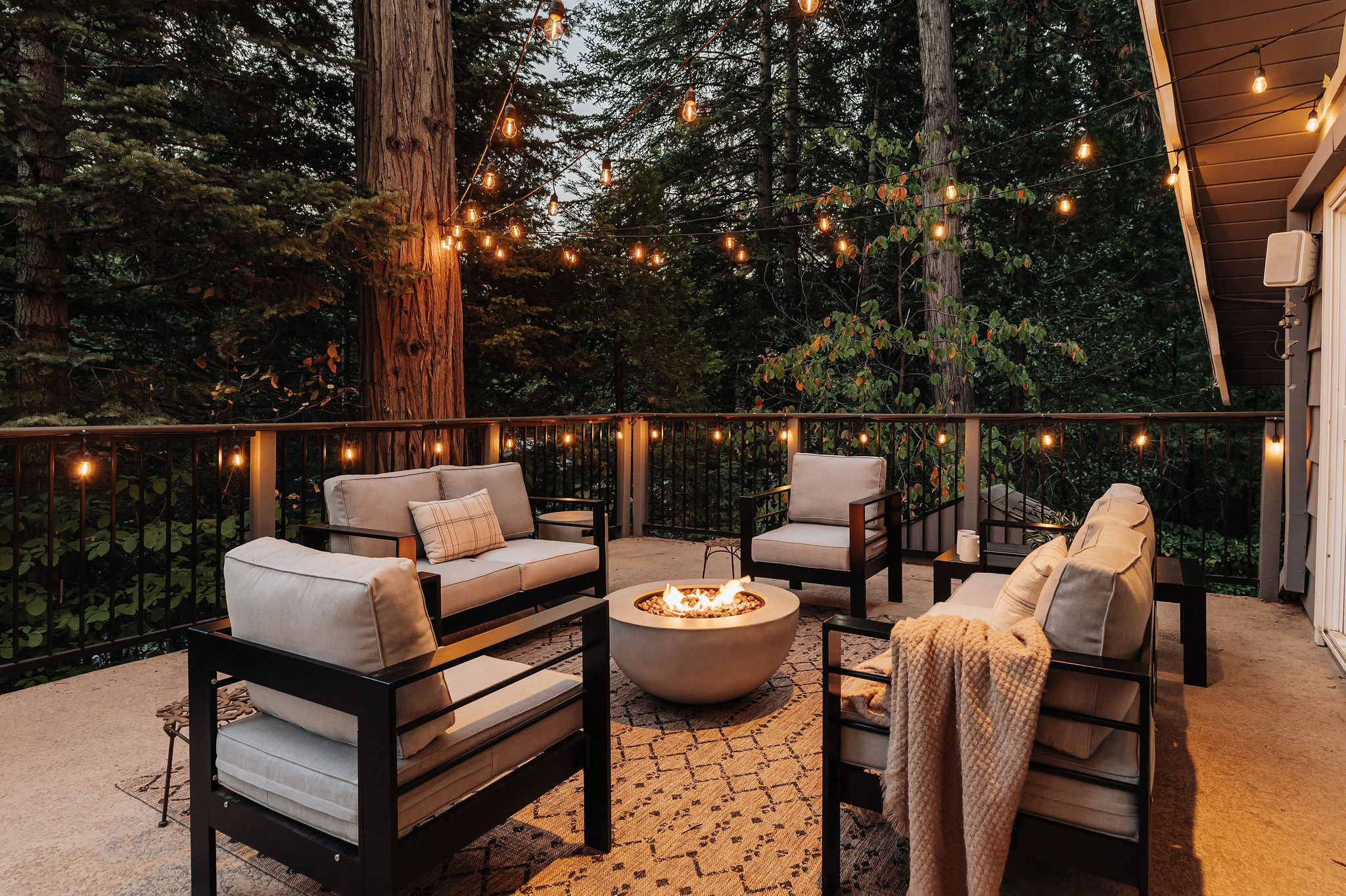 Forest-view deck with cozy fire pit lounge and glowing string lights