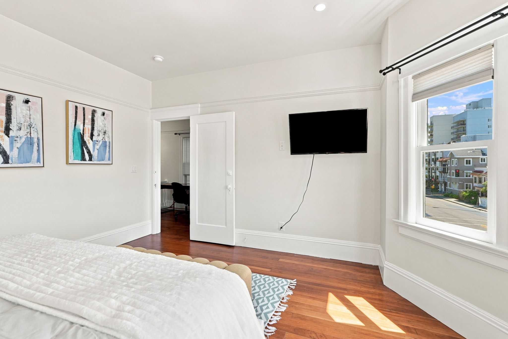 Bright bedroom with hardwood floors, city views, and wall-mounted TV