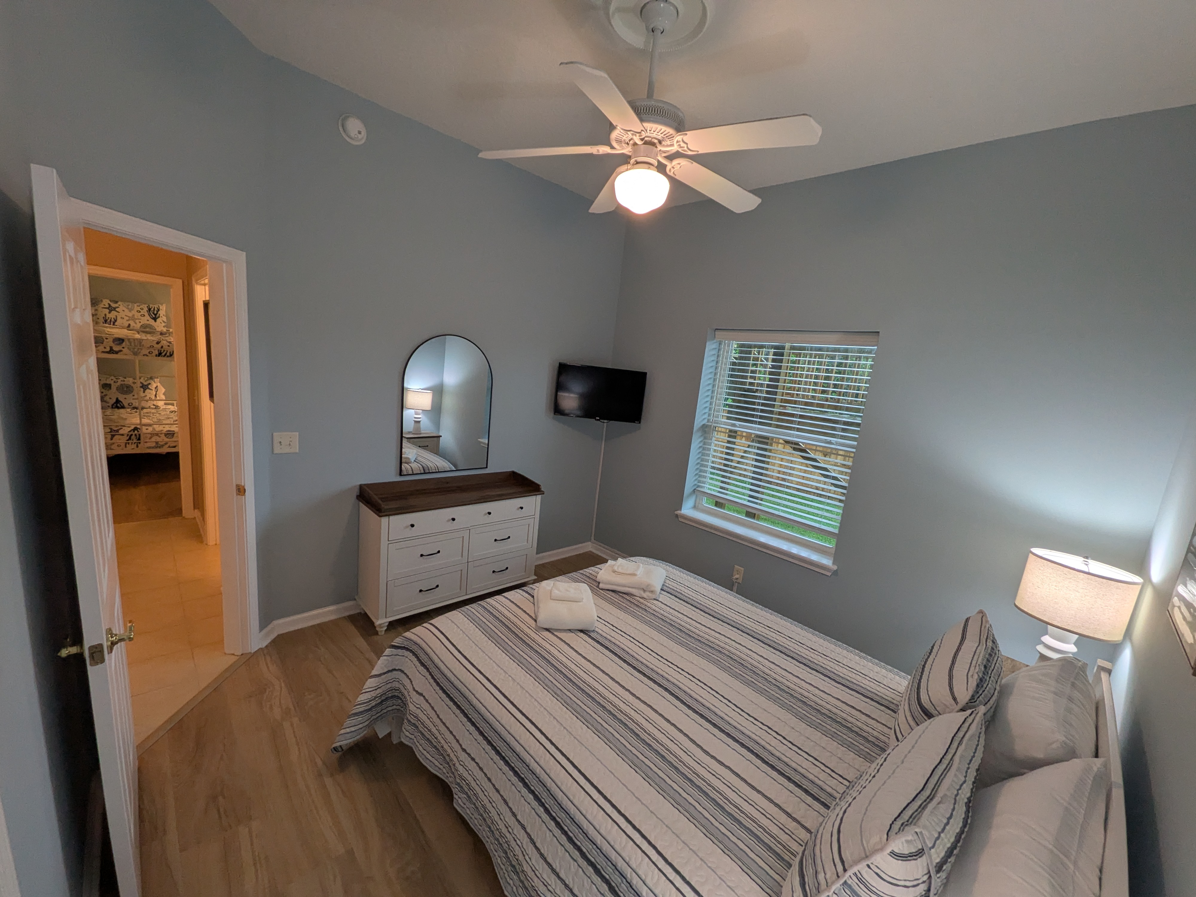 Bright, cozy bedroom with TV, ceiling fan, and easy bath access