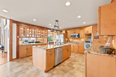 itchen with granite countertops and a center island with bar stools, stainless steel dishwasher, full-size refrigerator, wall oven, and cooktop, dark glass-front cabinets, pendant lighting over the island, and a wide pass-through to the dining area.