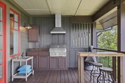 Grill dinner on the covered balcony with a full outdoor kitchen - stainless grill, prep counter, and a bar rail facing the ridgeline. Rain or shine, this is where the evening ends up.