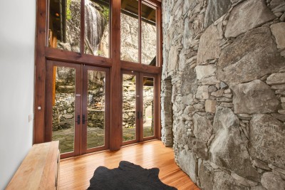 Even the front hall has a view: floor-to-ceiling glass doors open onto the stone courtyard where the waterfall spills down the cliff just outside.