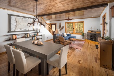 Cozy, open-concept living space where the farmhouse dining table sits just steps from the stone fireplace and sectional, gathered beneath a wood ceiling, built for big groups and long evenings together.